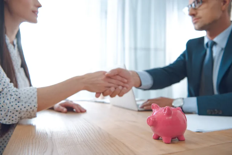Benefits of financing electrical upgrades in North Shore IL - 2 People in a business setting at a table. Both are shaking hands. Pink piggy bank in the foreground.